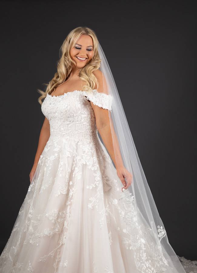 Model standing looking downwards wearing a long veil and an Alice Bridal Dress stocked by Roberta's Bridal, Burslem
